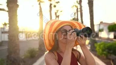 摄影女游客戴着一顶黄色的大帽子，在夕阳下美丽的热带风景中用相机拍照